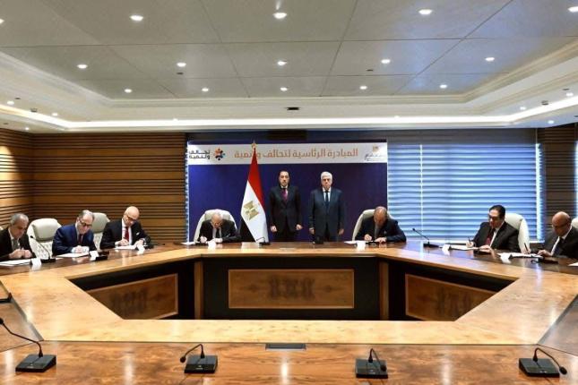 A group of people sitting around a table signing an agreement with the Egyptian flag in the background