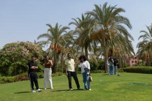 Males and females are standing on greenery surrounded by palm trees and trees