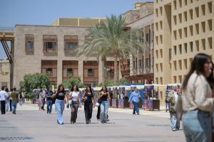 Males and females are walking in an open space. There are buildings around them