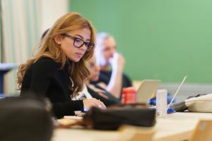 a girl with orange hair wearing black eye glasses and a black top sitting in a classroom