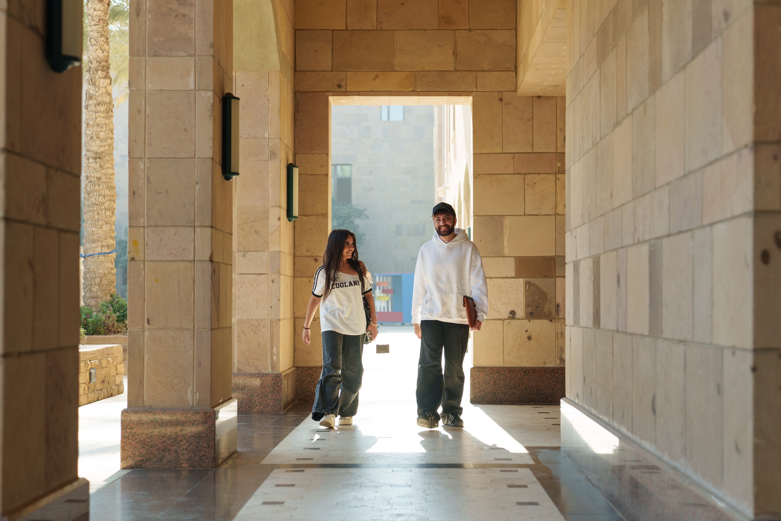 a girl and boy wearing white tshirts and blue jeans walking on campus