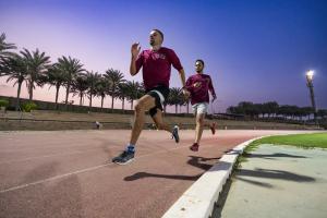 two male athletes running the track wearing maroon tshirts