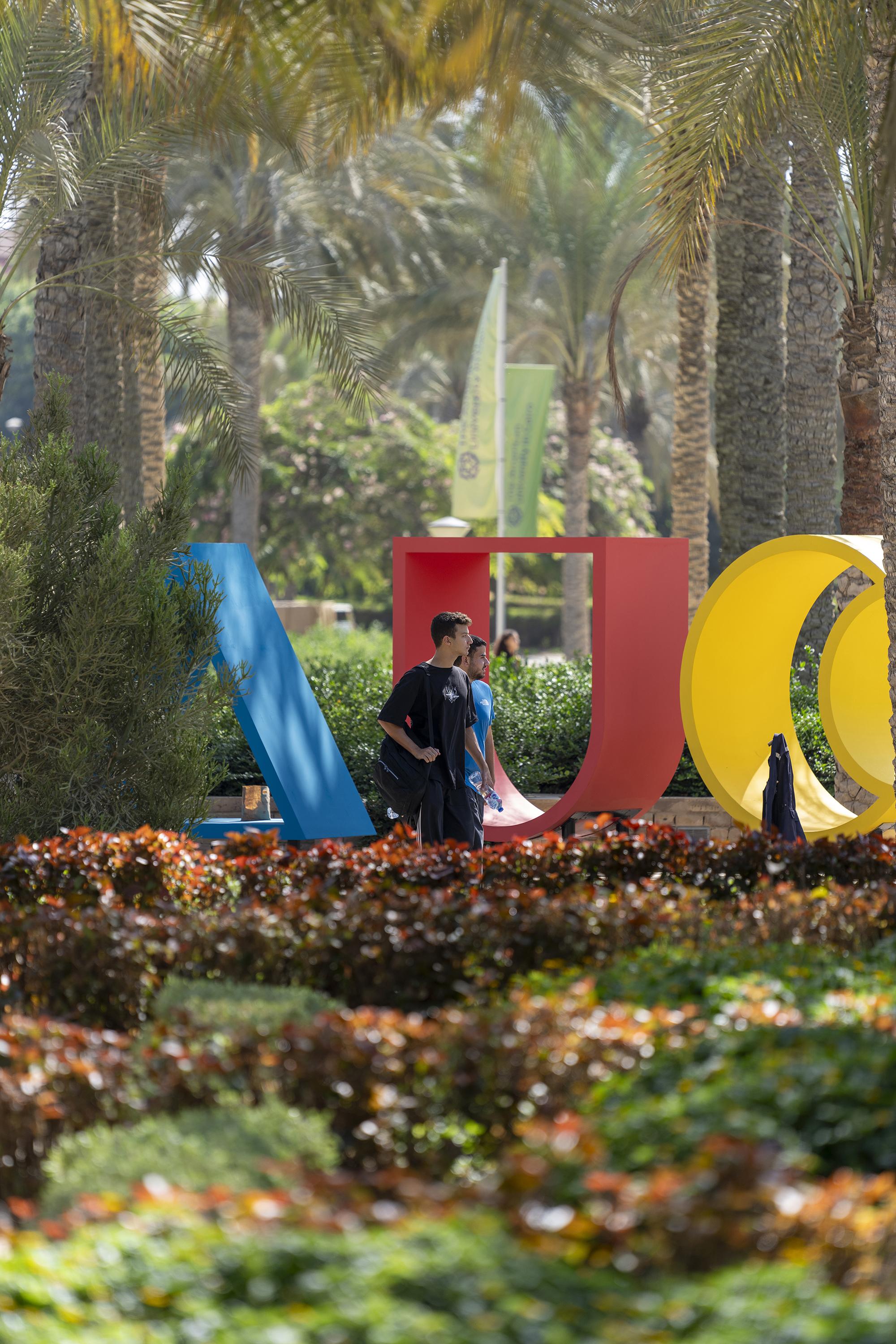 two students walking on campus with AUC monogram behind them