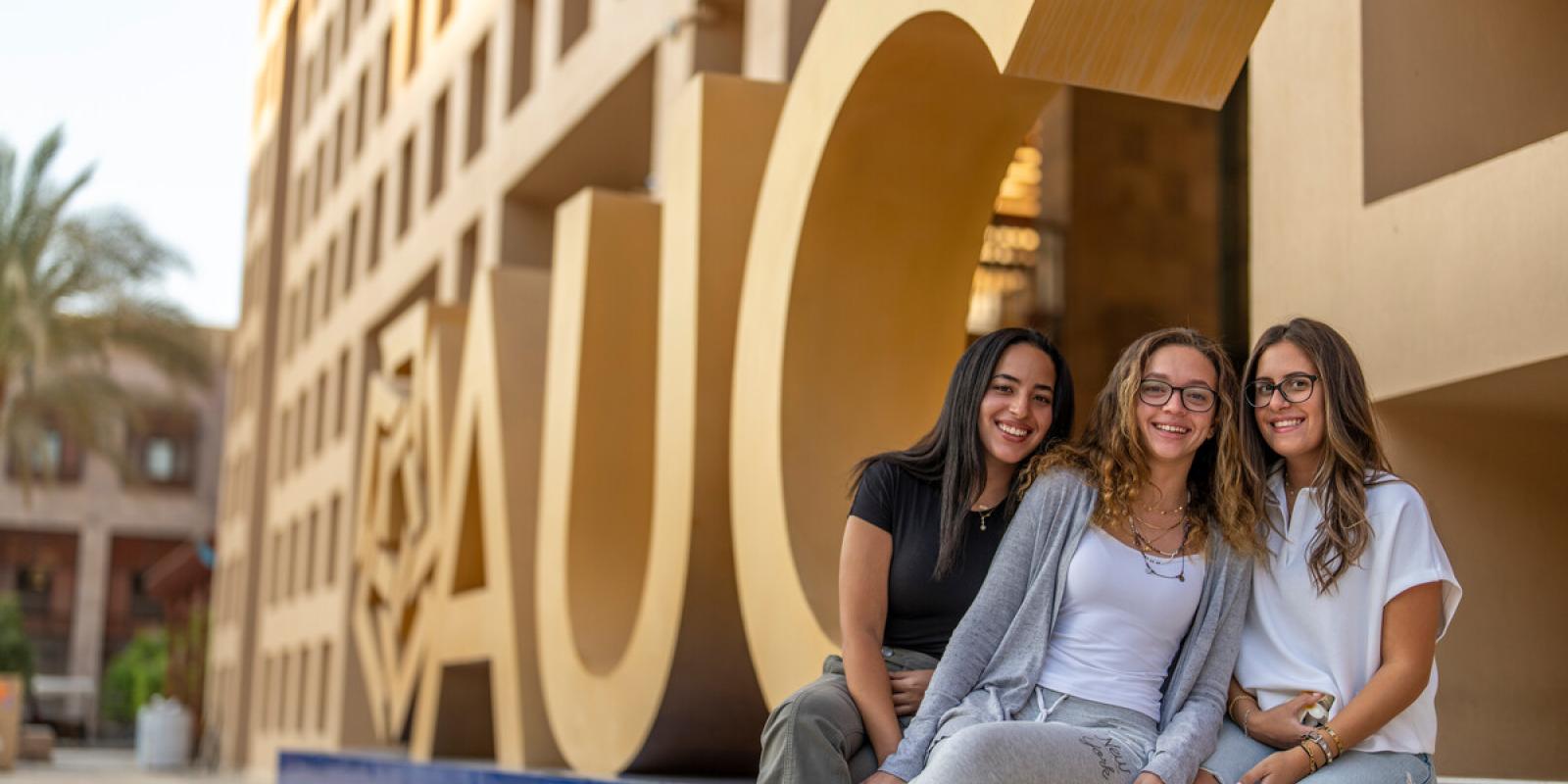 students sitting next to AUC logo in the Bartlett Plaza