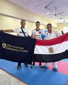 3 men standing with 2 flags, the Egyptian flag and AUC dark blue flag