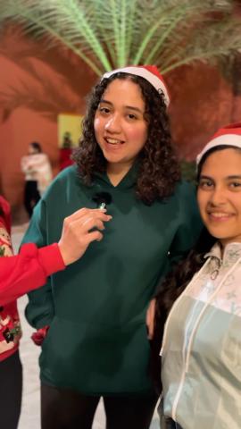 Two females are wearing Christmas hats and talking into a microphone