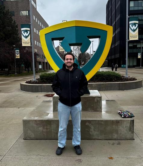A male is standing in the street and smiling. The area seems wet.