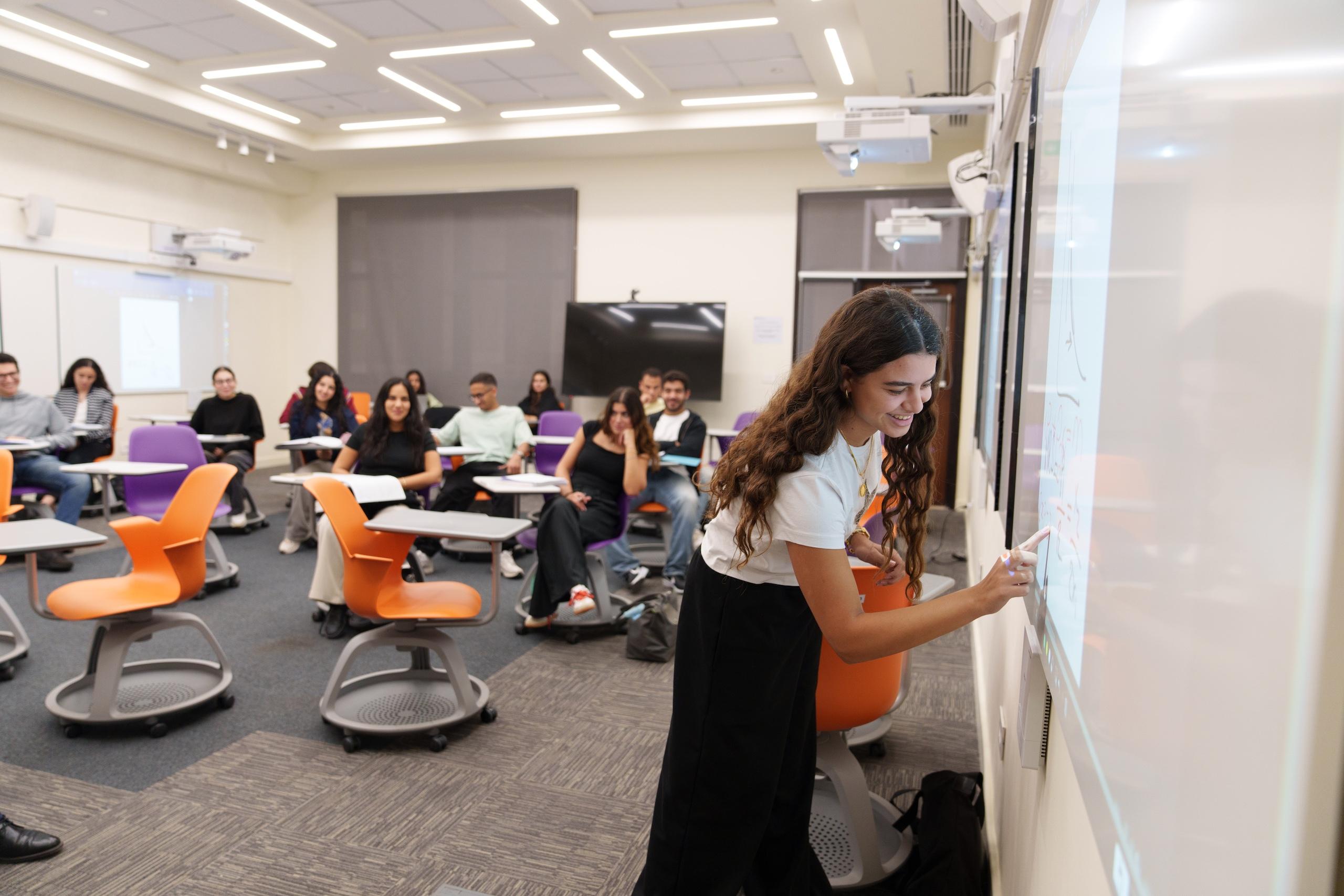 a girl in a classroom writing on the white smart board