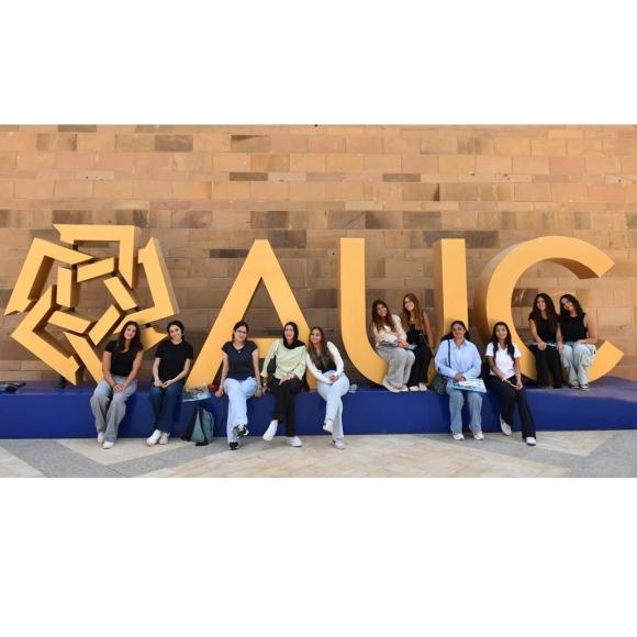 Females are sitting in front of the letters A U C