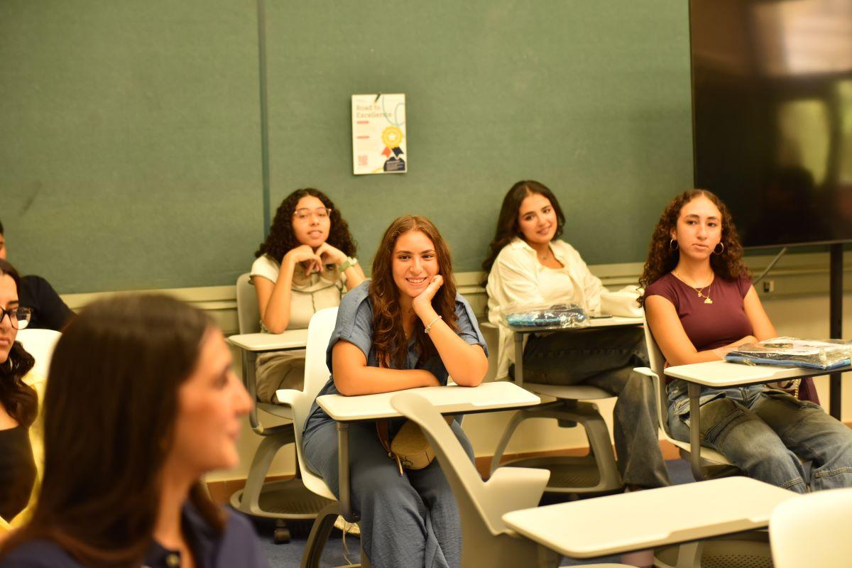 A bunch of students in a classroom listening to another student talk and they look interested.