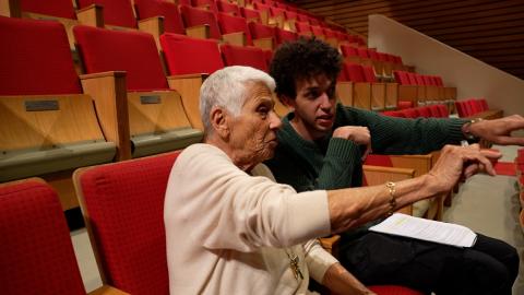 Former faculty Laila Saad is sitting with a male student in a theater pointing forward
