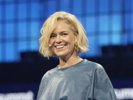 A woman is smiling. She is wearing an ear microphone