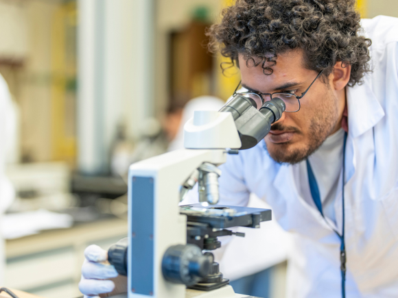A male student wearing a lab coat and looking into a microscope in a lab at AUC
