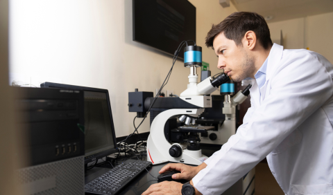 A scientist in a lab coat peers through a microscope.