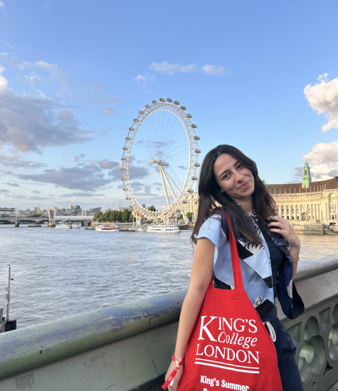 A female is standing in front of the London Eye. She is smiling and holding a bag that says "King's College London. King's Summer Program"