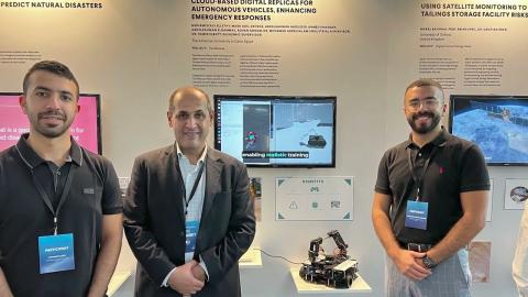 Three men standing next to each other, there are three screens ganging on the wall behind them